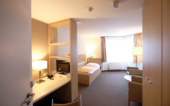 Modern eingerichtetes Einzelzimmer in der Schön Klinik mit Bett, Schreibtisch, Sesseln und Tageslicht