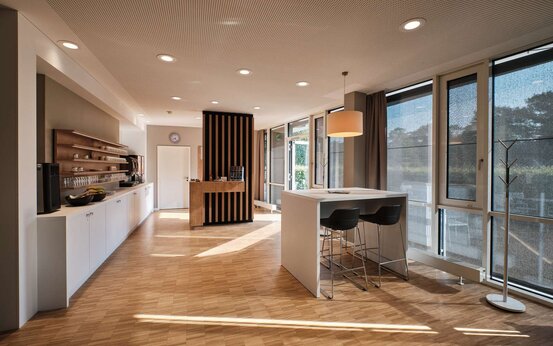 Heller Aufenthaltsbereich mit Hochtisch und Stühlen, Regalen und Fenstern