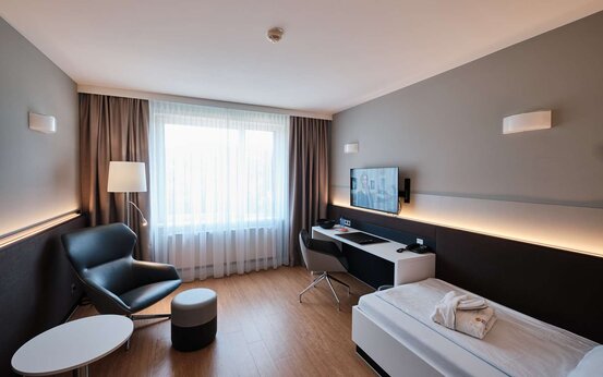 Einzelzimmer mit Bett, Schreibtisch, Sessel, Fernseher und Fenster