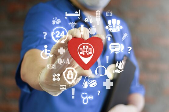Medizinisches Fachpersonal hält ein rotes Herz mit Klinik-Symbol, umgeben von Gesundheits-Icons