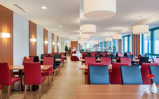 Modernes, helles Restaurant mit großen Panoramafenstern, roten und schwarzen Stühlen, Holztischen und Einzelblumenvasen