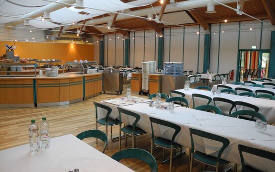 Heller, moderner Speisesaal mit gedeckten Tischen, grün-blauen Stühlen und großer Buffet-Theke in Klinik