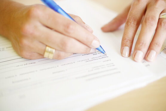 Nahaufnahme von Händen, die ein Patientenaufnahmeformular mit blauem Kugelschreiber ausfüllen