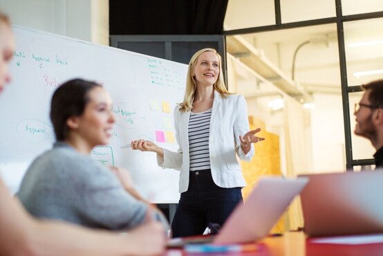 Vier Personen bei Teammeeting im modernen Büro, Frau präsentiert am Whiteboard, Fokus auf Zusammenarbeit