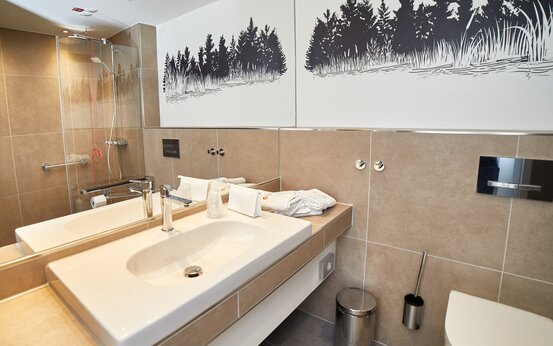 Barrierefreies, modernes Badezimmer mit bodengleicher Dusche, Haltegriff, wandhängendem WC und großem Spiegel