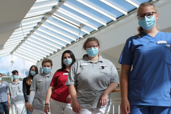 Gruppe von sieben medizinischen Fachkräften mit Masken steht gemeinsam in modernen, hellen Klinikflur