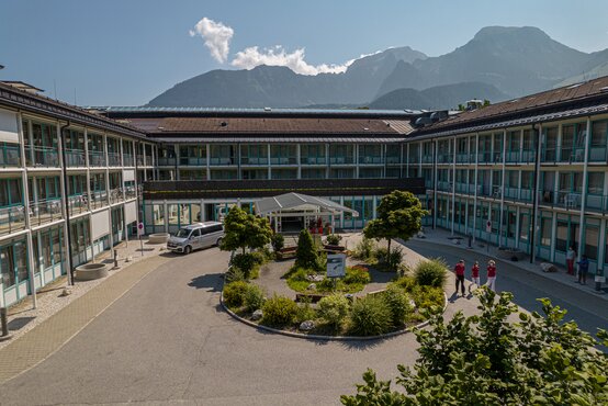 Schön Klinik Berchtesgadener Land mit begrüntem Innenhof, Balkonen und Alpenpanorama im Hintergrund.