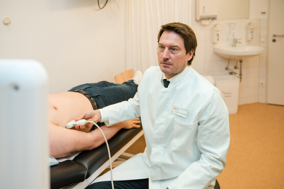 Arzt in weißem Kittel führt Ultraschalluntersuchung am Bauch eines Patienten im modernen Behandlungszimmer durch