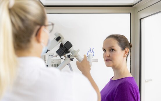 Ärztin führt mit medizinischem Gerät einen Lungenfunktionstest (Spirometrie) bei Patientin im Untersuchungsraum durch