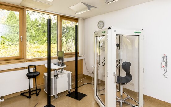 Heller Untersuchungsraum mit moderner Lungenfunktionskabine, Computerarbeitsplatz und medizinischer Ausstattung für Lungenfunktionstest