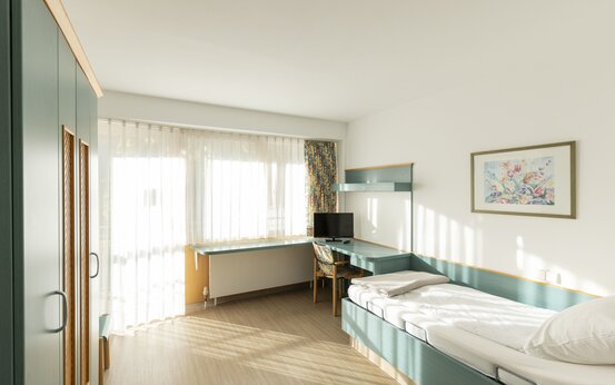 Helles Einzelzimmer mit Einzelbett, Schreibtisch, Flachbildfernseher, großem Fenster