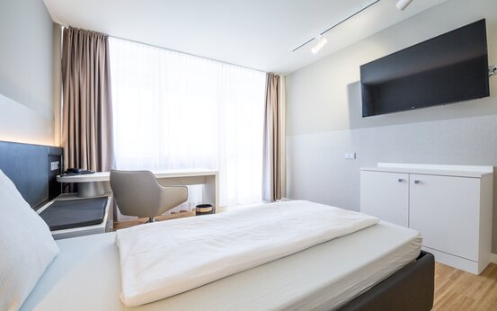 Komfortzimmer mit großem Bett, Schreibtisch am Fenster, Holzfußboden und Wand-TV