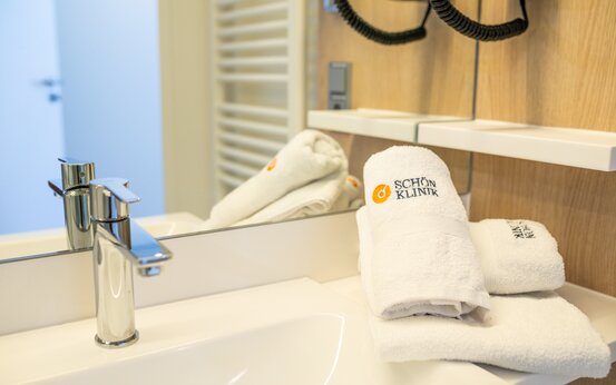 Badezimmer mit großem Spiegel, weißen Handtüchern „Schön Klinik“ und Handtuchheizkörper