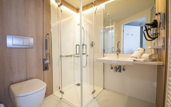 Badezimmer mit bodengleicher Dusche, Haltegriff, wandhängender Toilette und modernem Waschbecken