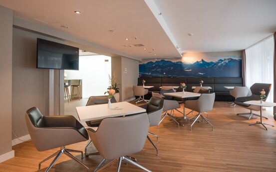 Moderner, heller Aufenthaltsraum mit Lounge-Sesseln, Blumenvasen und Alpenbild