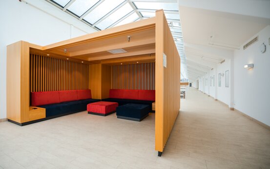 Heller, moderner Wartebereich mit Holz-Sitznische, roten und blauen Polstermöbeln und großen Fenstern 