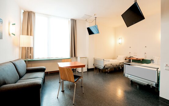 Modernes, helles Doppelzimmer mit zwei Pflegebetten, Sofa, Tisch und Fenster