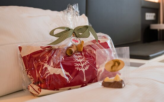 Geschenkset mit rotem Stoff und Rentiermotiv als Begrüßung auf Klinikbett im modernen Patientenzimmer