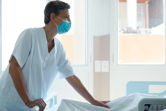 Pflegekraft mit OP-Maske am Krankenhausbett im hellen Patientenzimmer