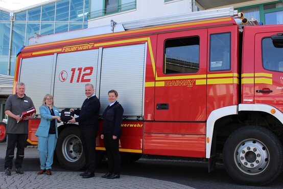 Vier Personen übergeben vor Feuerwehrfahrzeug Bad Staffelstein einen Defibrillator, feierliche Spendenübergabe, alle lächeln