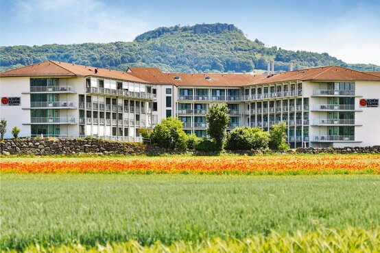 Modernes Hauptgebäude der Schön Klinik Bad Staffelstein im Grünen, umgeben von blühenden Wiesen, Feldern und Hügeln