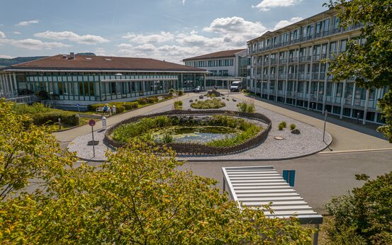 Schön Klinik Bad Staffelstein mit Glasfassade, Flachbau, Innenhof mit Teich, Rundweg, Bäumen und Parkplätzen
