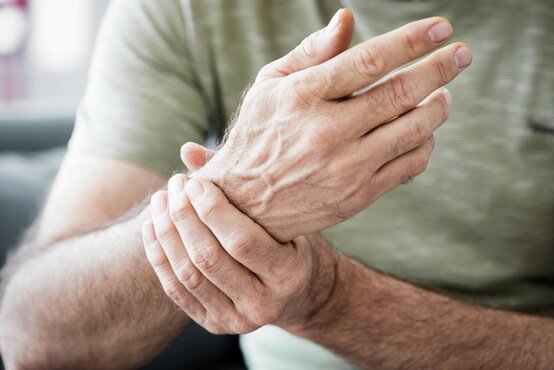 Nahaufnahme eines Mannes im hellgrünen T-Shirt, der mit der rechten Hand sein linkes Handgelenk umfasst