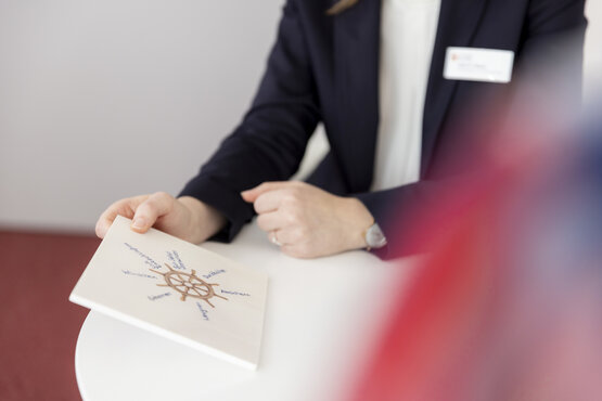 Psychotherapeutin im Gespräch mit Klient, hält Karte mit Steuerrad und lösungsorientierten Begriffen am Tisch