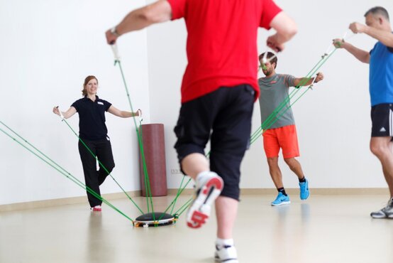 Gruppe von Erwachsenen trainiert unter Anleitung einer Physiotherapeutin mit grünen Widerstandsbändern