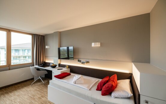 Modernes, barrierefreies Komfortzimmer in der Klinik mit großem Fenster, Balkonblick, Holzboden und stilvoller Einrichtung