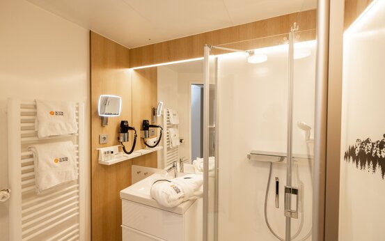 Modernes, barrierefreies Klinik-Komfortzimmer-Bad mit Handtüchern, Dusche und Kosmetikspiegel