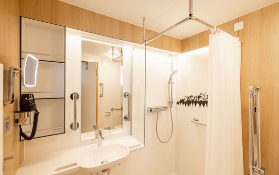 Badezimmer mit ebenerdiger Dusche, Haltegriffen, Sitzmöglichkeit und modernem Holzdekor