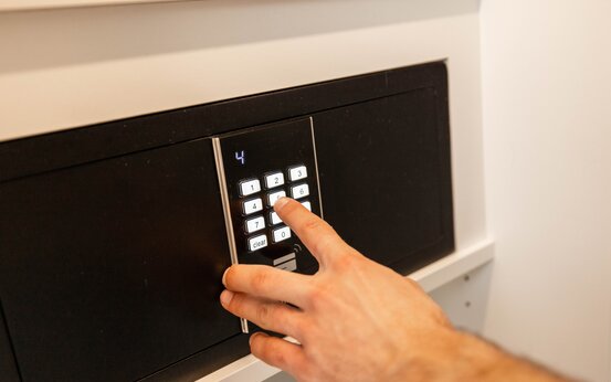 Hand gibt Zahlencode auf beleuchtetem digitalen Safe im Komfortzimmer für Privatpatienten im Krankenhaus ein
