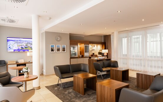 Helles, modern eingerichtetes Zimmer mit schwarzen Sesseln, Holztischen, Kaffeemaschine