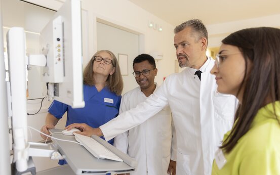 Ärzteteam und Pflegepersonal bei Visite betrachten gemeinsam Patientendaten am Computer
