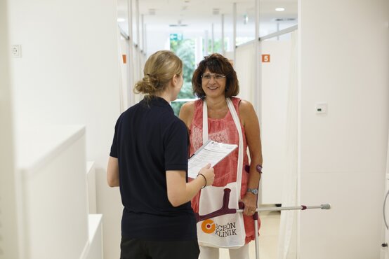 Patientin mit Gehhilfen wird von medizinischer Fachkraft im Klinikflur begrüßt