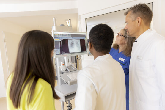 Interdisziplinäres Team aus Arzt und Pflegekraft bei Visite am Patientenbett in moderner Klinik