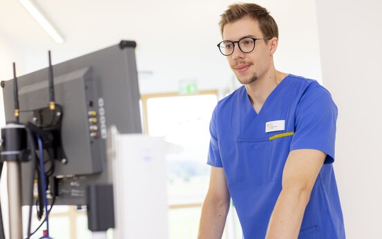 Pfleger mit Brille dokumentiert Patientendaten am Computer auf moderner Station, digitale Pflege im Krankenhausalltag