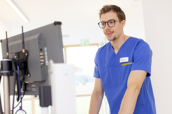 Pfleger mit Brille dokumentiert Patientendaten am Computer auf moderner Station, digitale Pflege im Krankenhausalltag