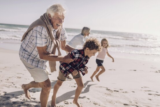 Älteres Paar und zwei Kinder laufen lachend barfuß am sonnigen Strand entlang