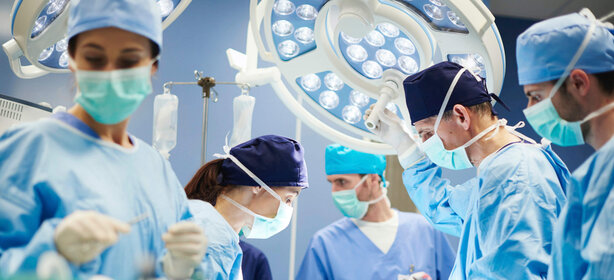 Mehrere Chirurgen und medizinisches Fachpersonal in OP-Kleidung führen gemeinsam eine Operation im modernen Operationssaal durch