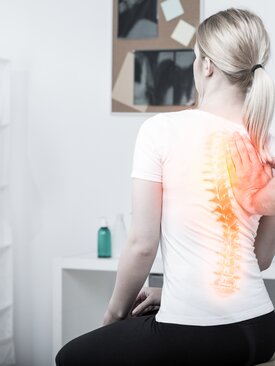 Junge Frau bei orthopädischer Rückenuntersuchung, Arzt markiert schmerzhaften Bereich der Wirbelsäule