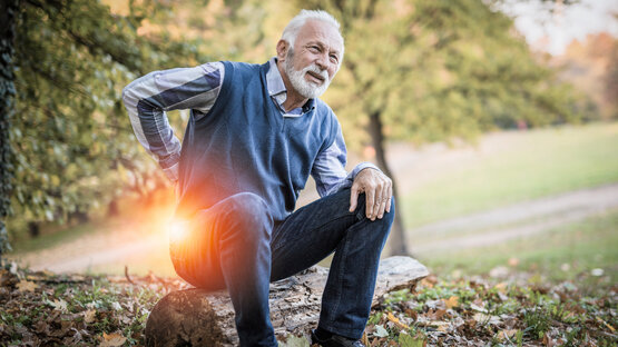 Älterer Mann hält sich mit schmerzverzerrtem Gesicht den unteren Rücken, Markierung am Lendenwirbelbereich