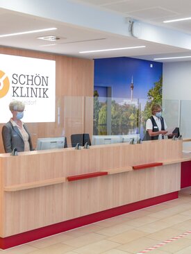 Moderner, barrierefreier Empfangsbereich der Schön Klinik Düsseldorf mit Holztheke, Plexiglas, Masken und Computerarbeitsplätzen