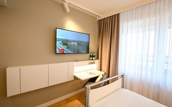Wahlleistungszimmer in der Klinik mit Einzelbett, Schreibtisch, Flachbildfernseher und großen Fenstern mit Tageslicht