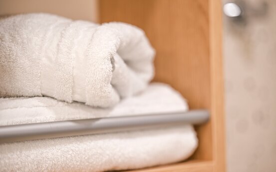 Zwei weiße, sauber gefaltete Handtücher auf Holzregal im Klinik-Badezimmer