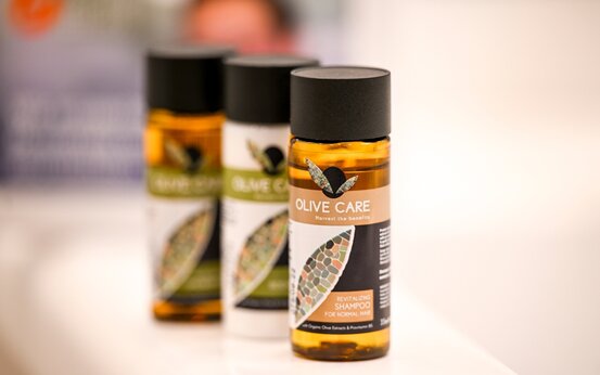 Drei handliche Pflegeprodukte „Olive Care“ auf weißer, barrierefreier Ablage im hellen Klinikbad, leicht erreichbar und hygienisch