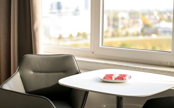 Helle, moderne Lounge-Ecke mit dunkelgrauem Sessel, weißem Tisch und Biscoff-Keksen vor großem Fenster