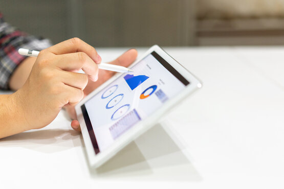 Hand mit Eingabestift zeigt auf Tablet mit farbigen Kreis- und Liniendiagrammen