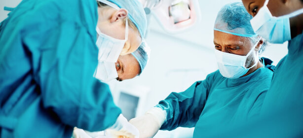 Chirurgisches Team aus vier Ärztinnen und Ärzten bei einer Operation im modernen Operationssaal, alle tragen sterile OP-Kleidung, Masken und Hauben